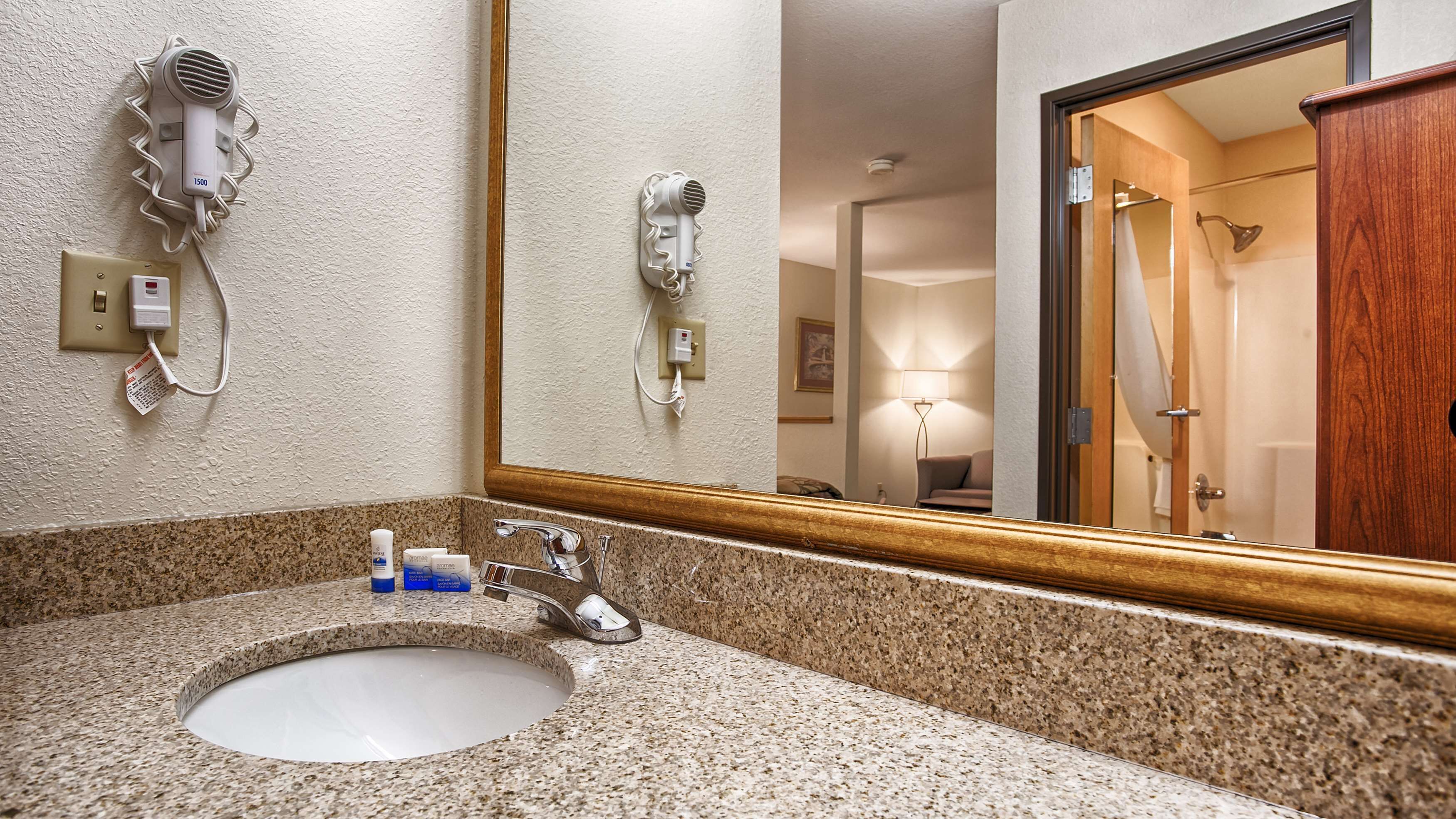 A bathroom with a granite countertop, a sink, a mirror, and two wall-mounted hair dryers.
