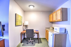Una kitchenette pequeña con microondas, un refrigerador compacto, un escritorio con silla y una lámpara.