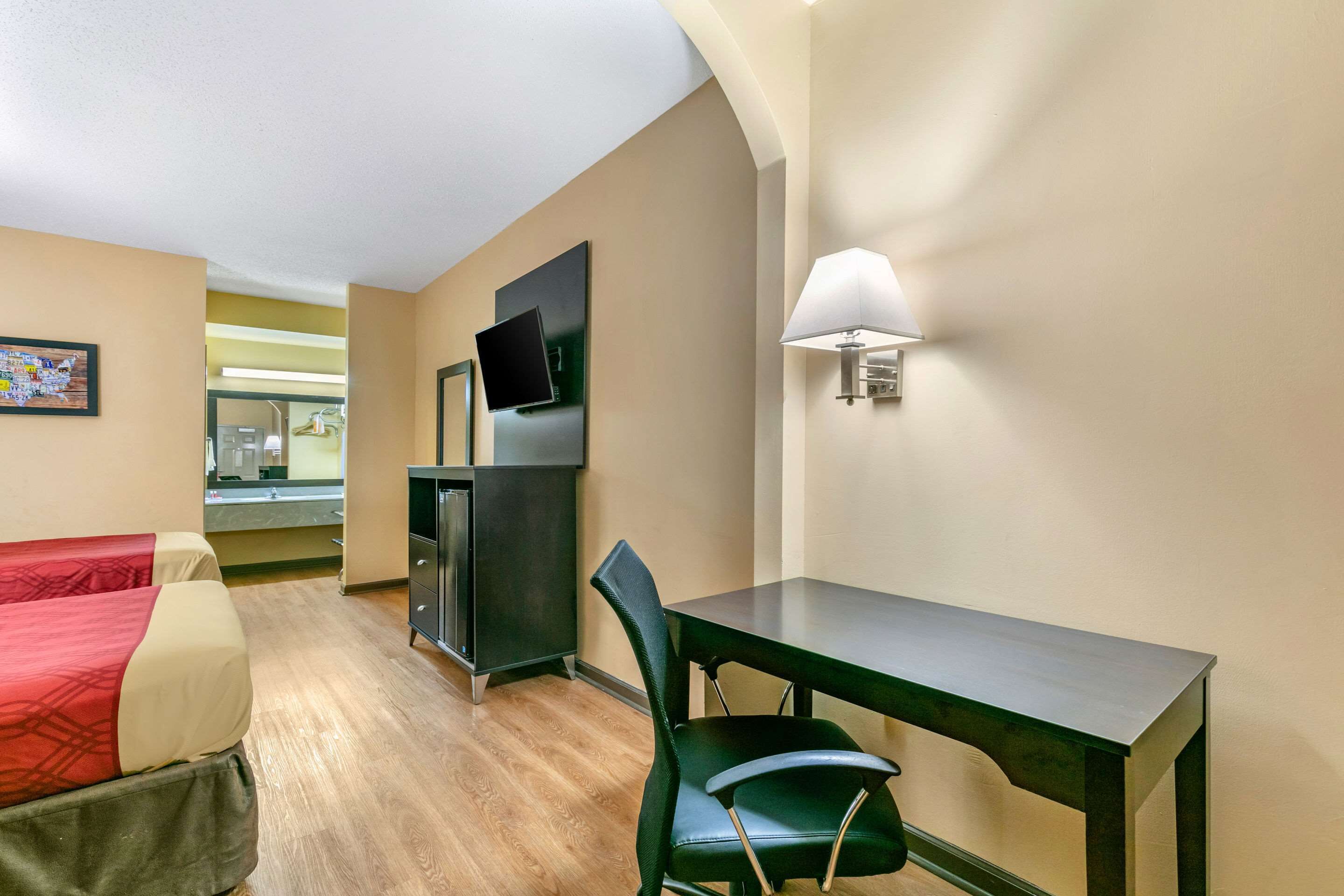 Una habitación de hotel con una cama, un escritorio, una silla, un televisor, una lámpara y un espejo.