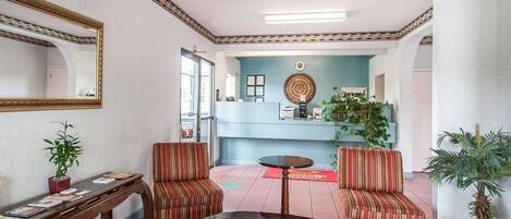 A lobby with a reception desk, two striped armchairs, a small table, a mirror, and a potted plant.