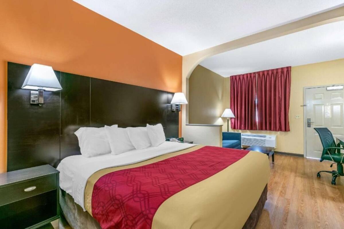 Ein Hotelzimmer mit einem Bett, zwei Nachttischlampen, einem Schreibtisch mit Stuhl und einem Vorhangfenster.