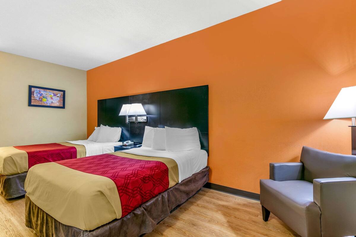 Ein Hotelzimmer mit zwei Betten, einem Schlafsofa, einem Nachttisch und einer Wandlampe.