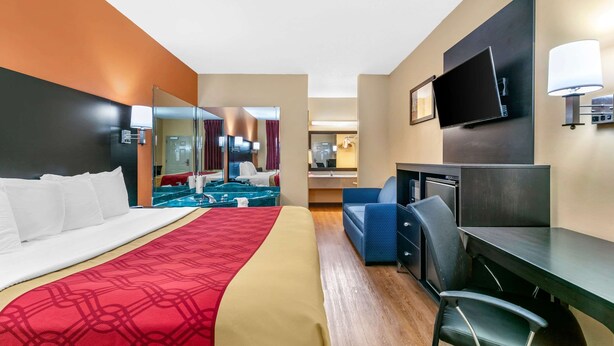 A hotel room with a bed, a desk, a chair, a TV, and a bathroom visible through a glass door. - Econo Lodge Northport near University (Northport)