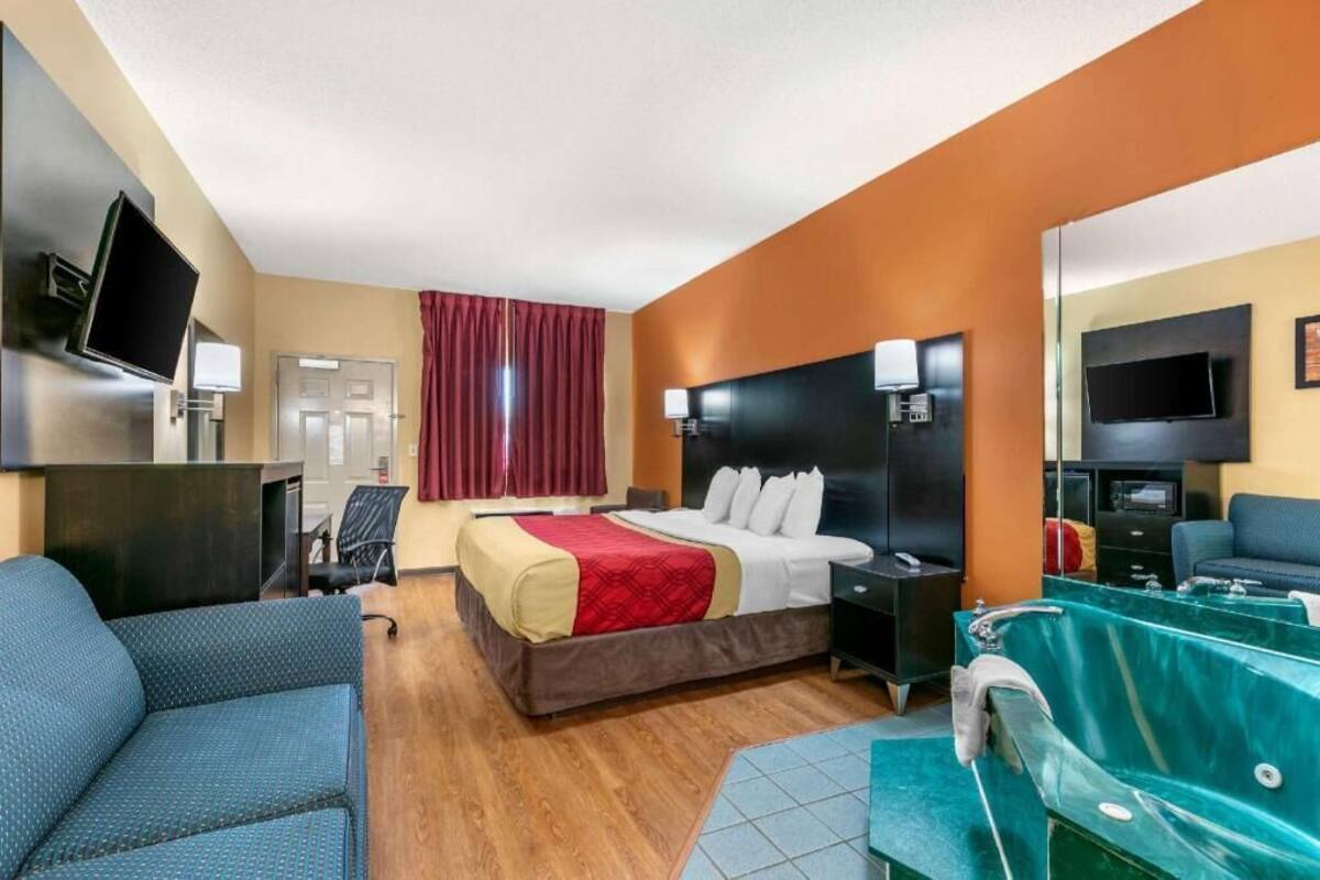 Ein Hotelzimmer mit Bett, Schreibtisch, Stuhl, Fernseher und einem Badezimmer mit Badewanne sowie einem Spiegel.