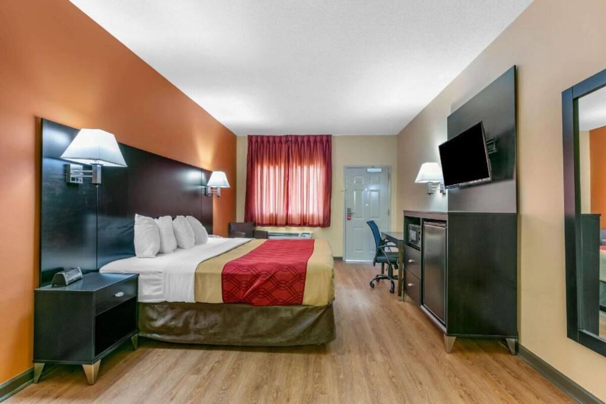 Ein Hotelzimmer mit Bett, Nachttischen, Schreibtisch, Stuhl, Fernseher und einem fenster mit Vorhängen.