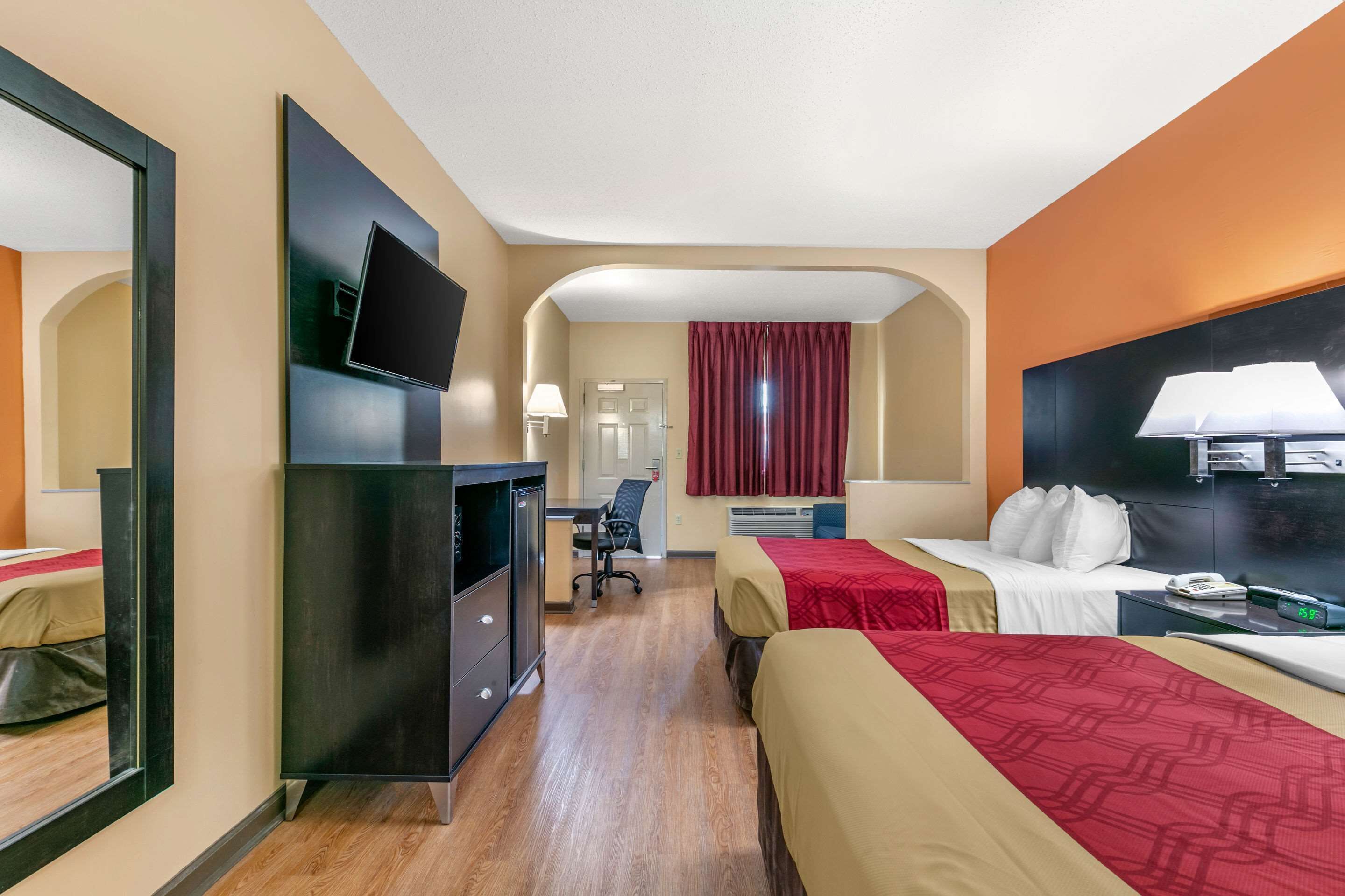 A hotel room with a desk, two beds, a TV, and a mirror.