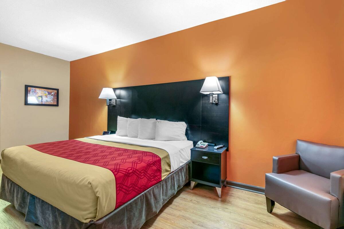Ein Hotelzimmer mit Bett, Nachttisch, Sessel und zwei Wandlampen.