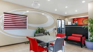 A modern dining area with a table and chairs, a potted plant, and a red sofa. - Econo Lodge Northport near University (Northport)