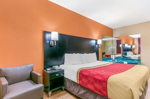 A hotel room with a large bed, a nightstand, a chair, and a mirror.