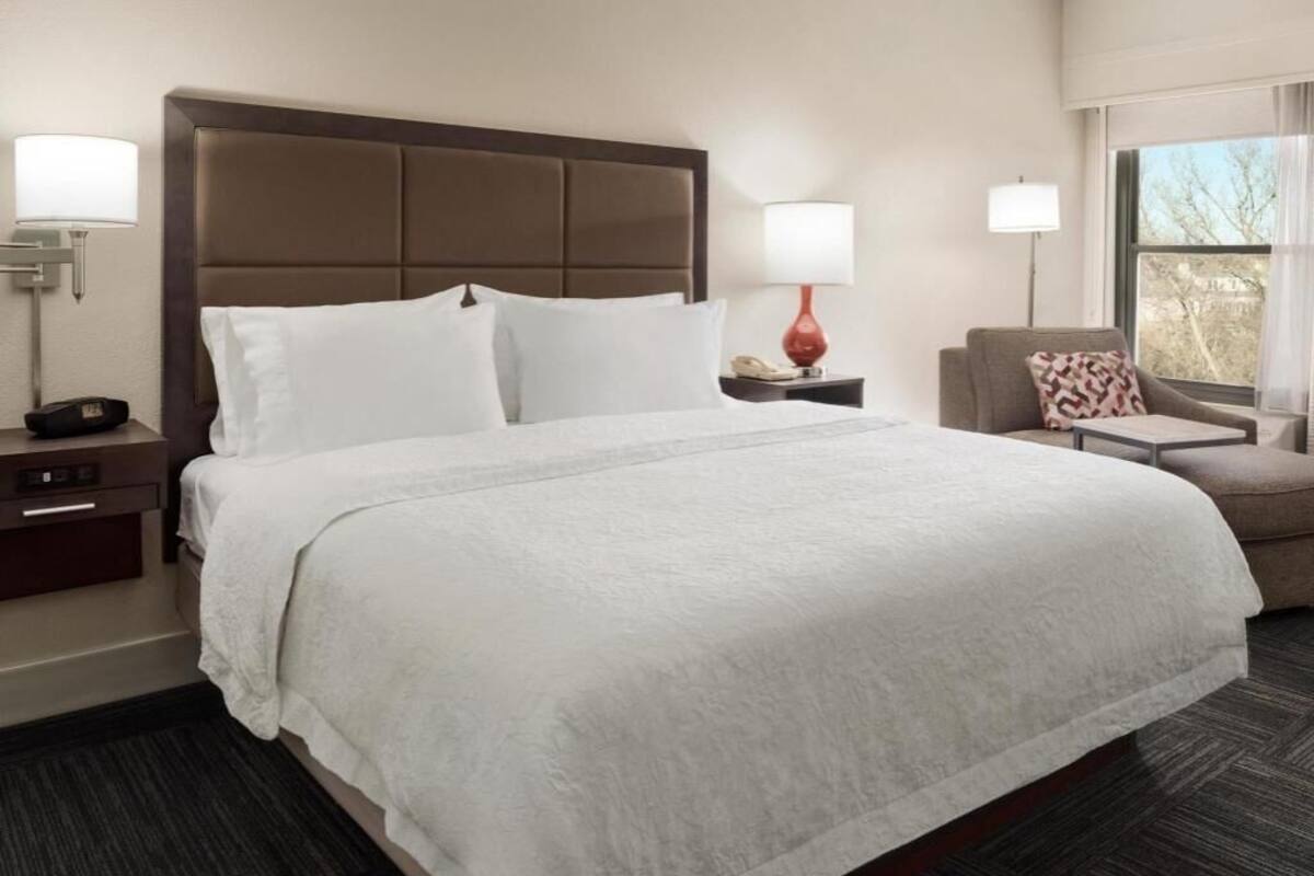 A hotel room with a large bed, two bedside tables, a chair, and a window.