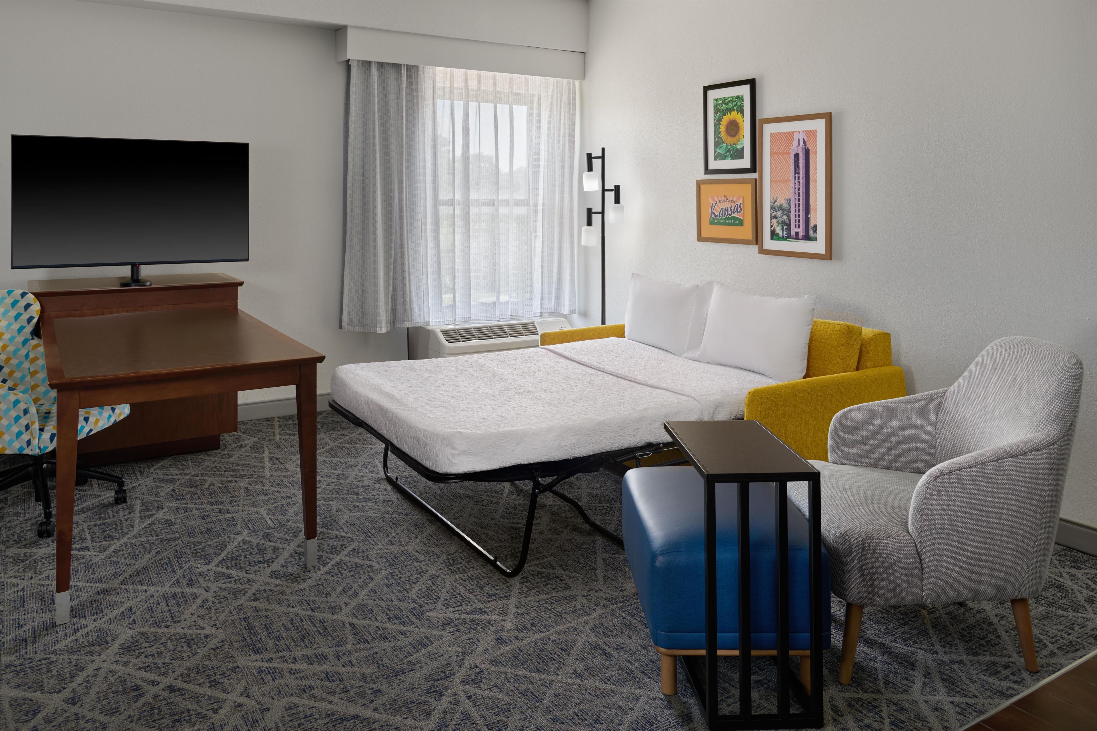 A hotel room with a bed, a desk, a chair, a TV, and a window with curtains.
