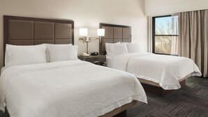 Habitación de hotel con dos camas, una mesita de noche con teléfono y una ventana con cortinas.
