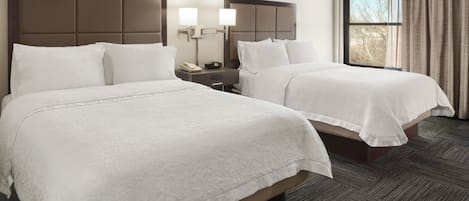 A hotel room with two beds, a nightstand with a phone, and a window with curtains.