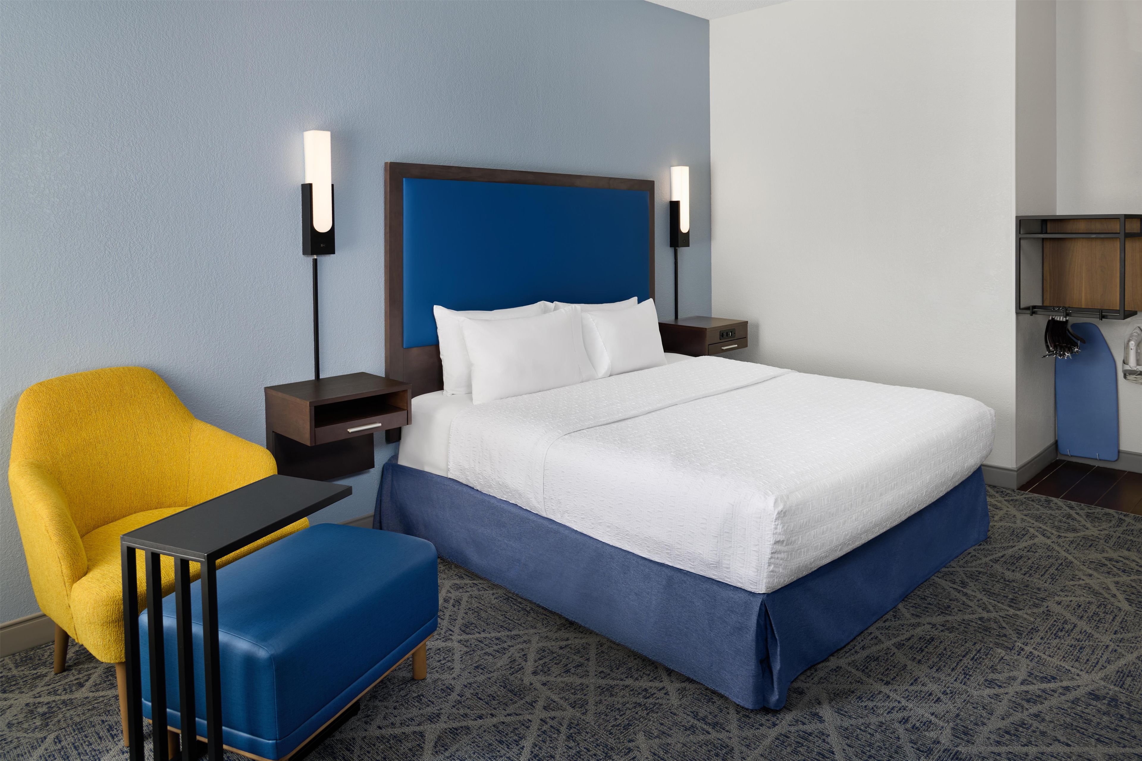 Una habitación de hotel con cama, mesita de noche, silla y escritorio.