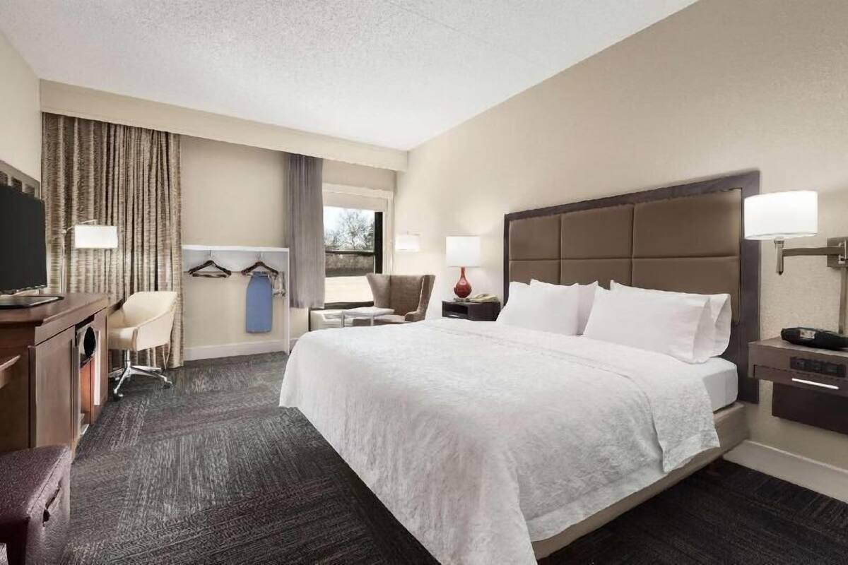 A hotel room with a large bed, a desk with a chair, a TV, and a window with curtains.