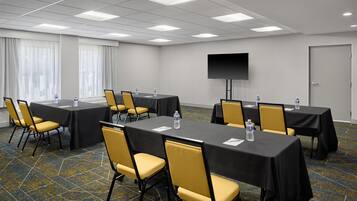 A conference room with tables, chairs, a flat-screen TV, and a door.
