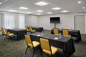 A conference room with tables, chairs, a flat-screen TV, and a door. - Hampton Inn Lawrence (Lawrence)