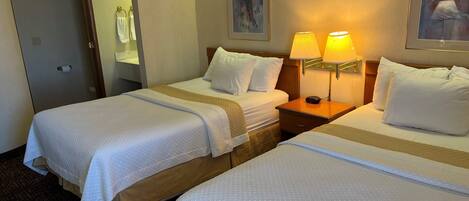 Une chambre d’hôtel avec deux lits, une table de chevet avec une lampe, un tableau au mur et une porte avec un porte-serviettes.