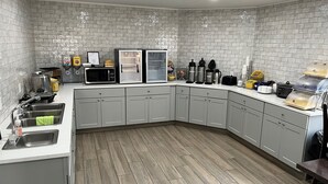 Eine moderne Küche mit grauen Schränken, einer Edelstahl-Spüle, einer Mikrowelle, einem Kühlschrank und verschiedenen Geräten auf der Arbeitsfläche.