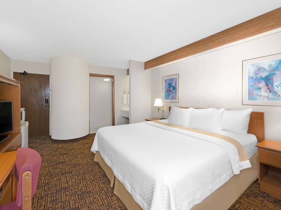 Habitación de hotel con una cama grande, un escritorio, una silla, un televisor y una puerta que da a otra habitación.