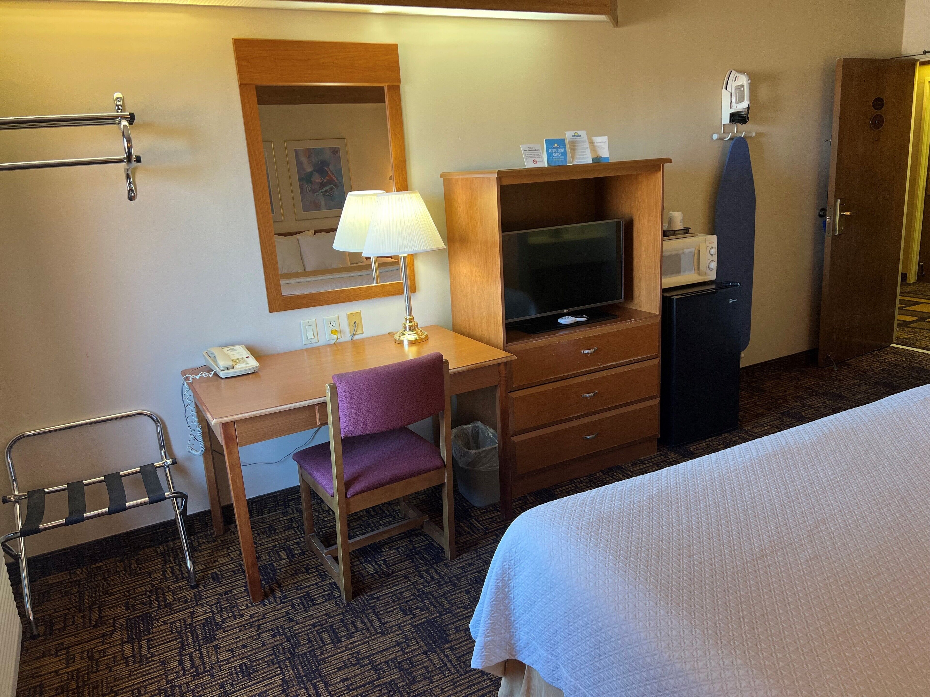 Habitación de hotel con escritorio, silla, televisor, minibar y cama.