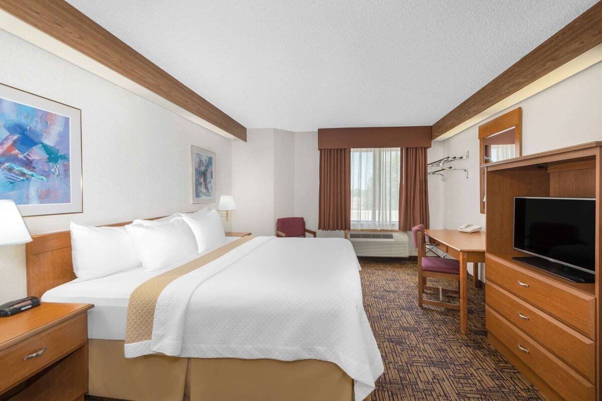 A hotel room with a bed, desk, TV, and a painting on the wall.