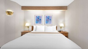 Ein Hotelzimmer mit einem großen Bett, zwei Nachttischen mit Lampen und zwei gerahmten Kunstwerken an der Wand.