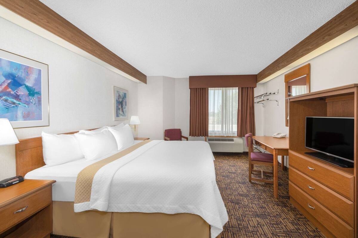 A hotel room with a large bed, a desk, a television, and a chair.