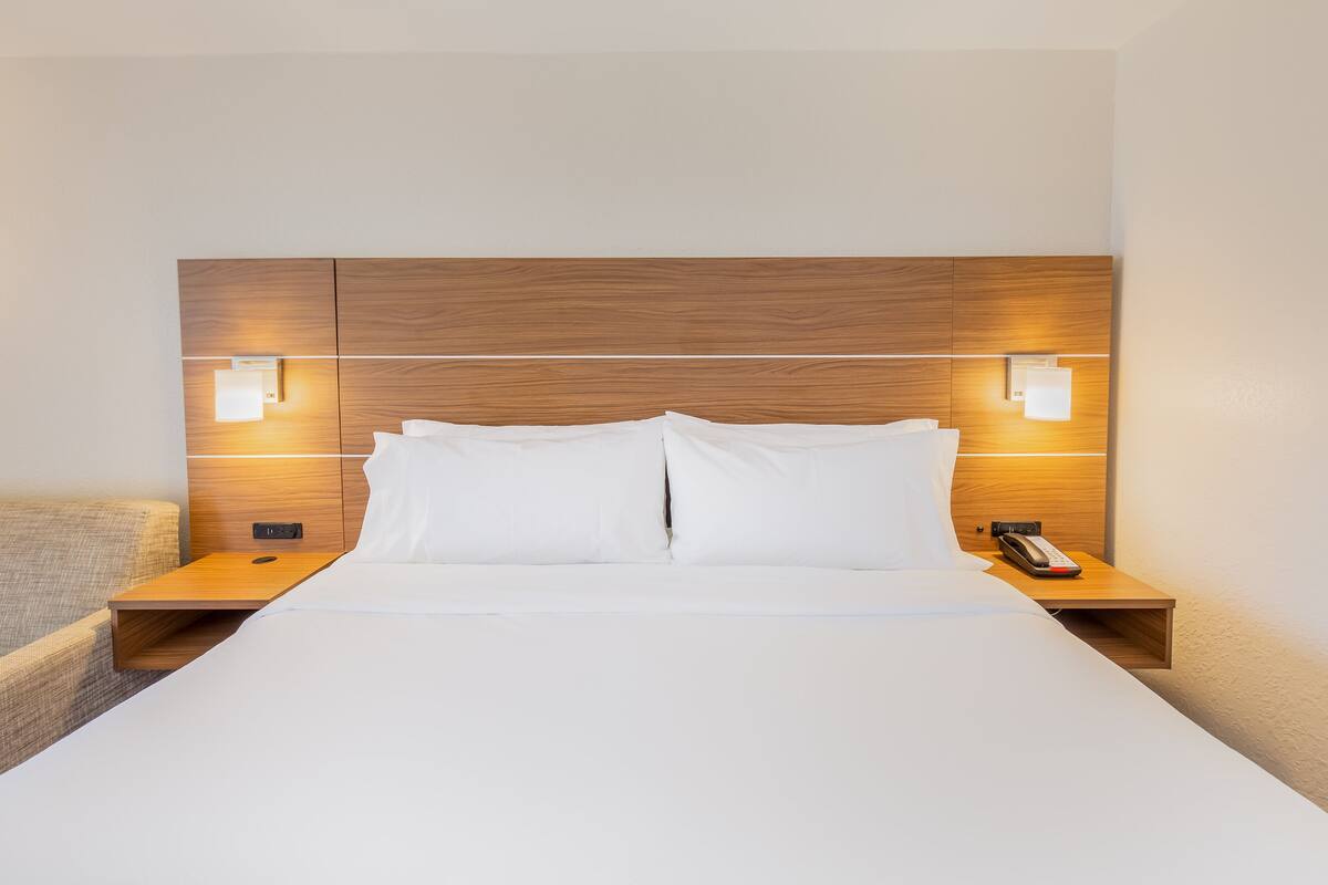 Habitación de hotel con cabecera de madera, ropa de cama blanca y lámparas de noche.