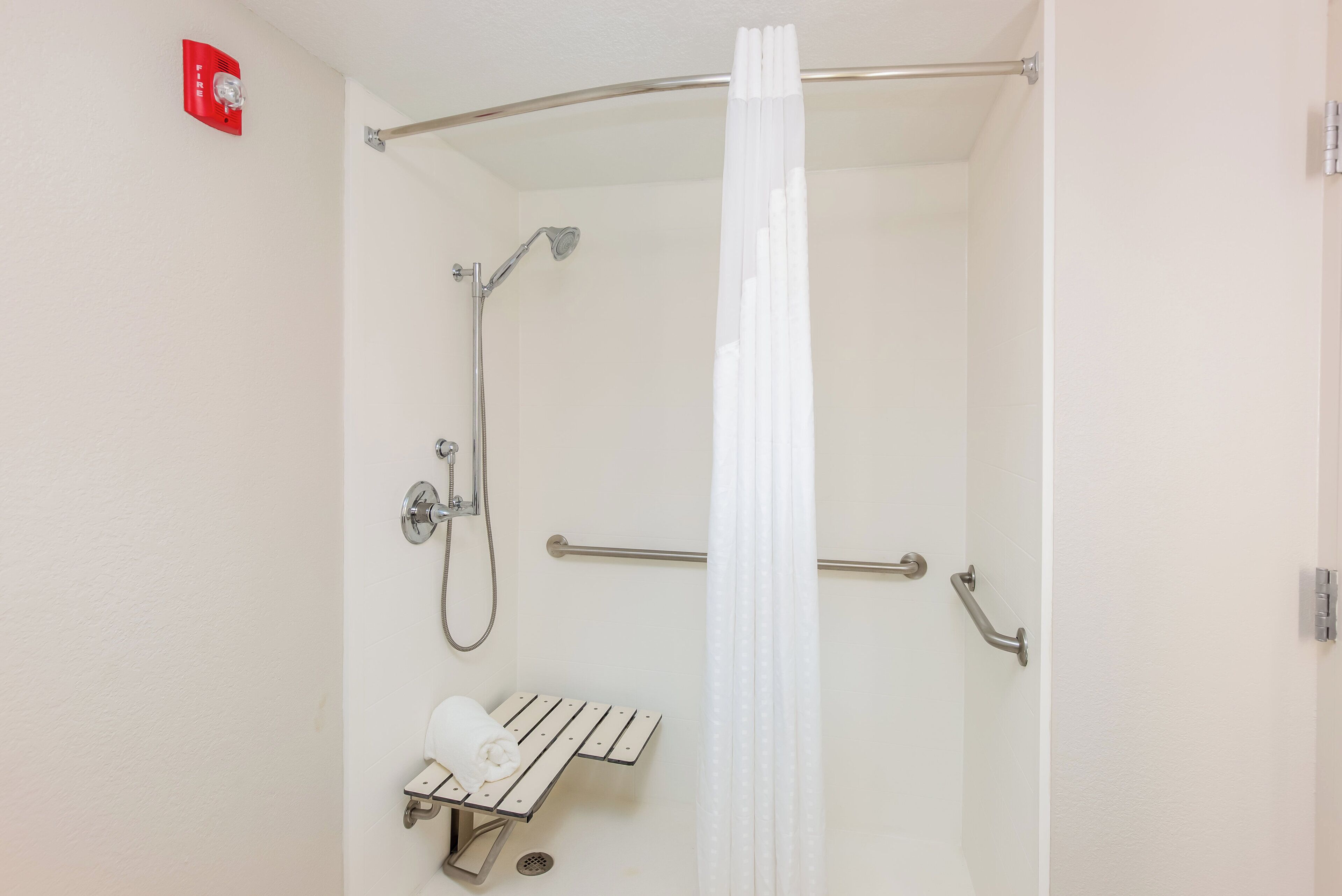 A shower with a handheld showerhead, a handheld showerhead, a towel rack, and a safety rail.
