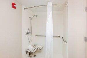 A shower with a handheld showerhead, a handheld showerhead, a towel rack, and a safety rail.