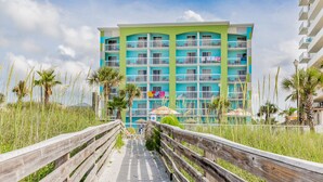 A multi-story hotel with balconies, a wooden boardwalk leading to the entrance, and palm trees in the foreground. - Holiday Inn Express Orange Beach by IHG (Orange Beach)