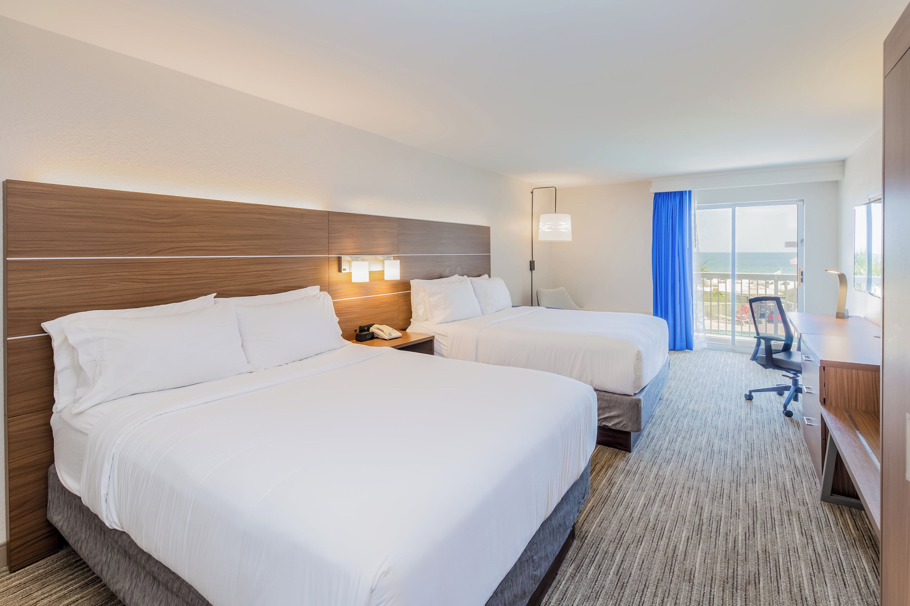 Habitación de hotel con dos camas, un escritorio, una silla, un teléfono y vista al océano.