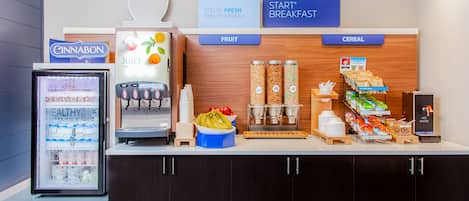 Una barra de desayuno con dispensador de bebidas refrigeradas, estación de zumos y exhibición de cereales.