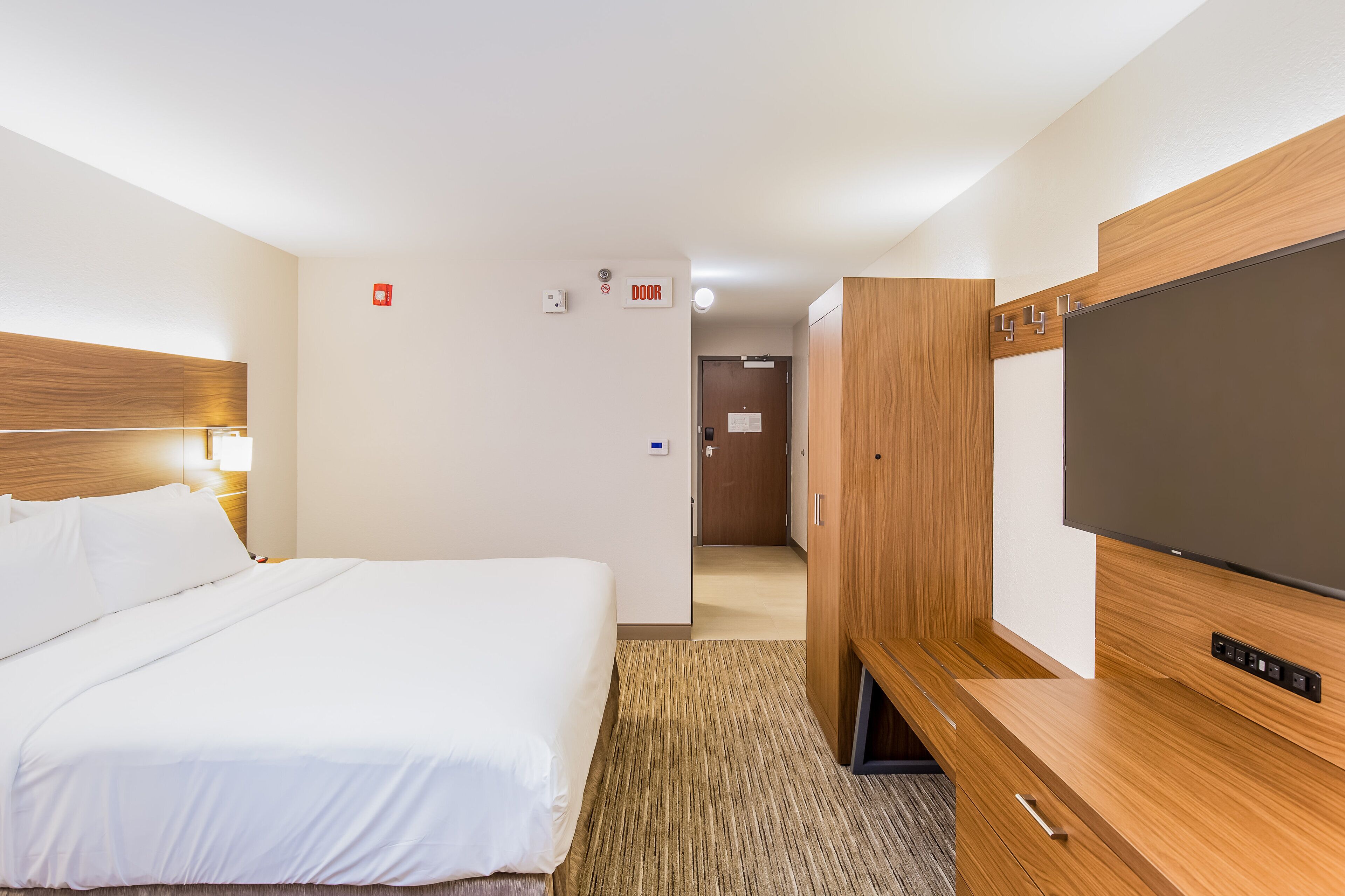 A hotel room with a large bed, a TV, wooden furniture, and a door with a sign.