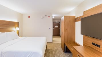 A hotel room with a large bed, a TV, wooden furniture, and a door with a sign.