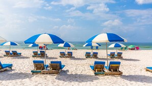 A beach with rows of blue and white beach umbrellas and lounge chairs, some labeled with names. - Holiday Inn Express Orange Beach by IHG (Orange Beach)