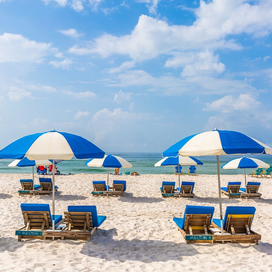 A beach with rows of blue and white beach umbrellas and lounge chairs, some labeled with names.