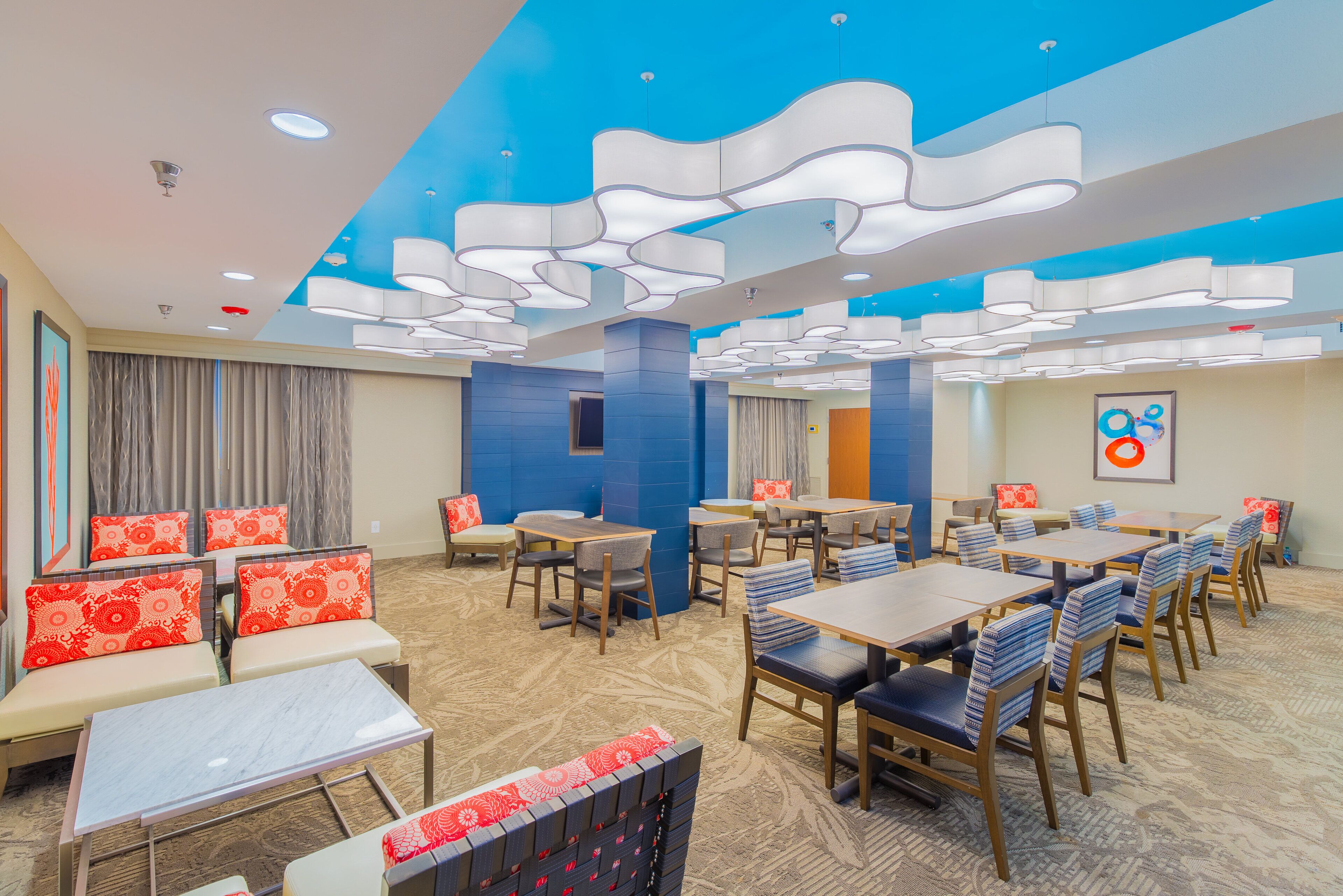 A hotel lobby with multiple seating areas, including sofas and tables, and a ceiling with unique light fixtures.