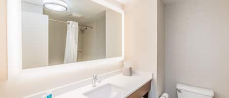 A bathroom with a white sink, mirror, and toilet. There is a towel rack and a shower curtain visible in the background.
