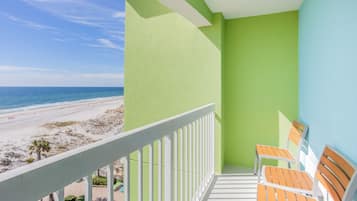 A balcony with a view of the beach, a pool, and two wooden chairs.
