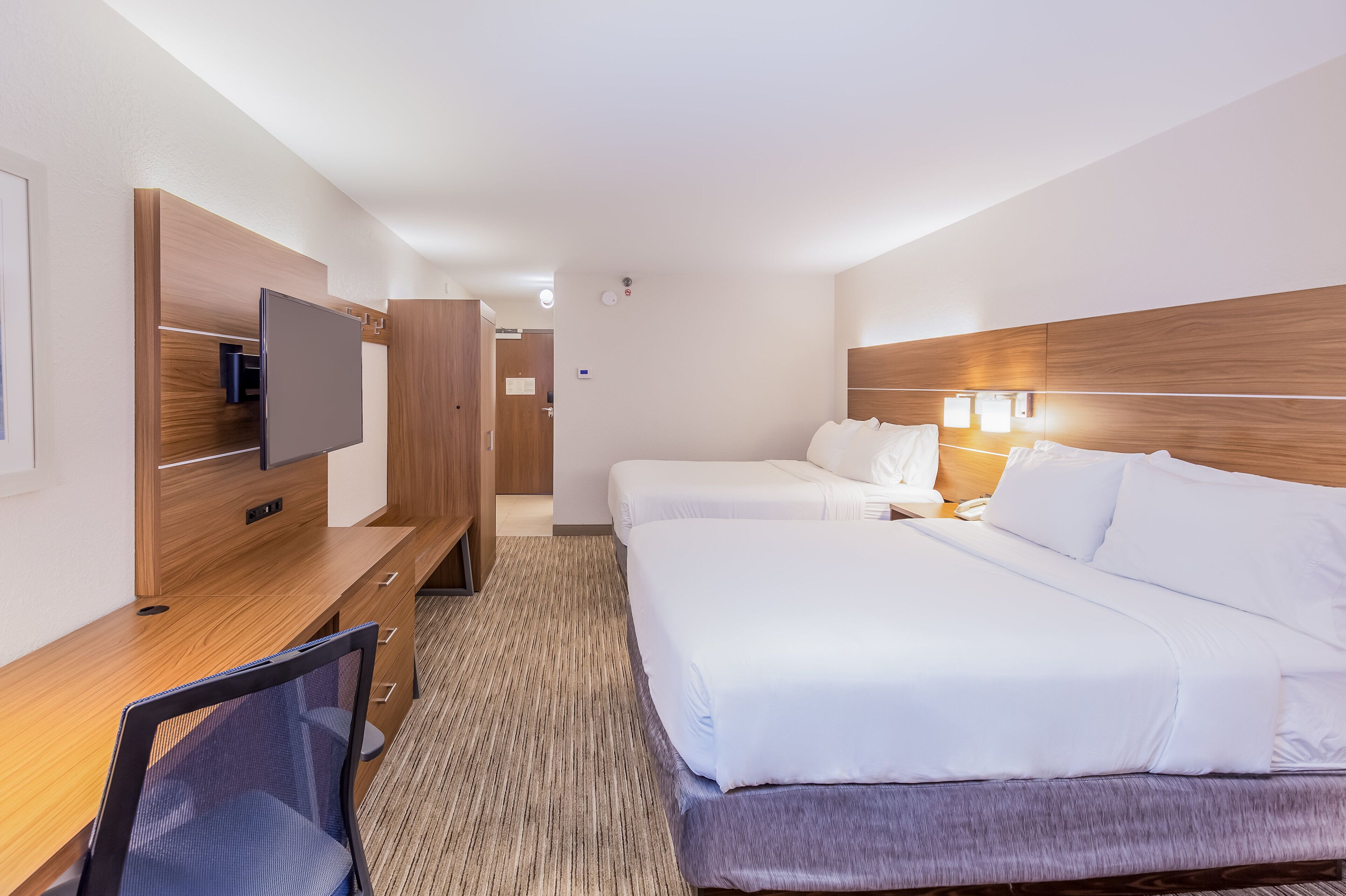 Habitación de hotel con escritorio de madera, televisor de pantalla plana, dos camas y piso alfombrado.
