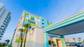 A Holiday Inn Express building with a modern design, featuring a prominent green and white color scheme, a covered parking area, and palm trees in front.