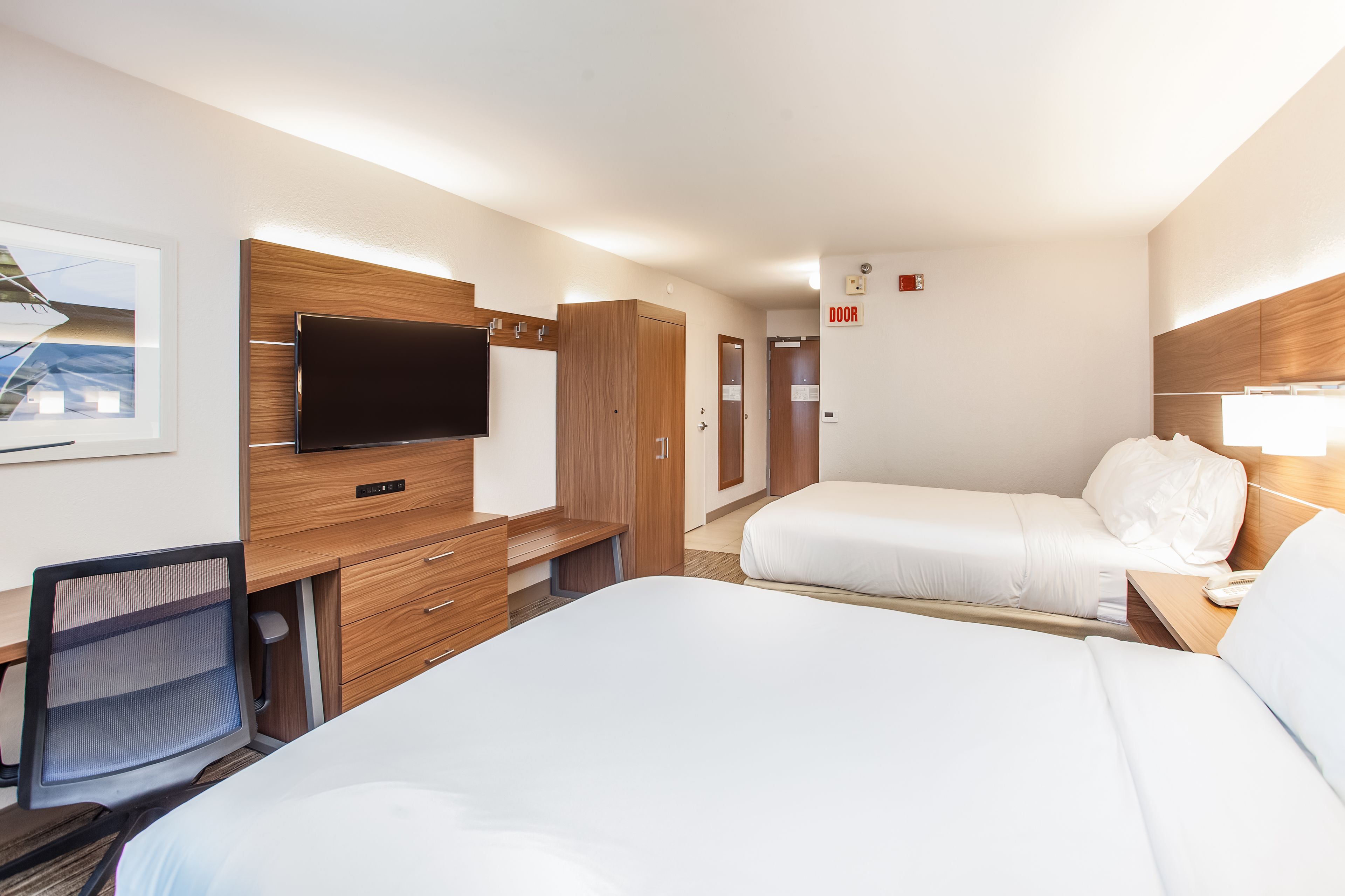 A hotel room with a bed, a desk, a chair, a TV, and a door.