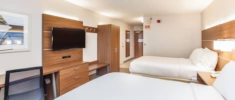 A hotel room with a bed, a desk, a chair, a TV, and a door.