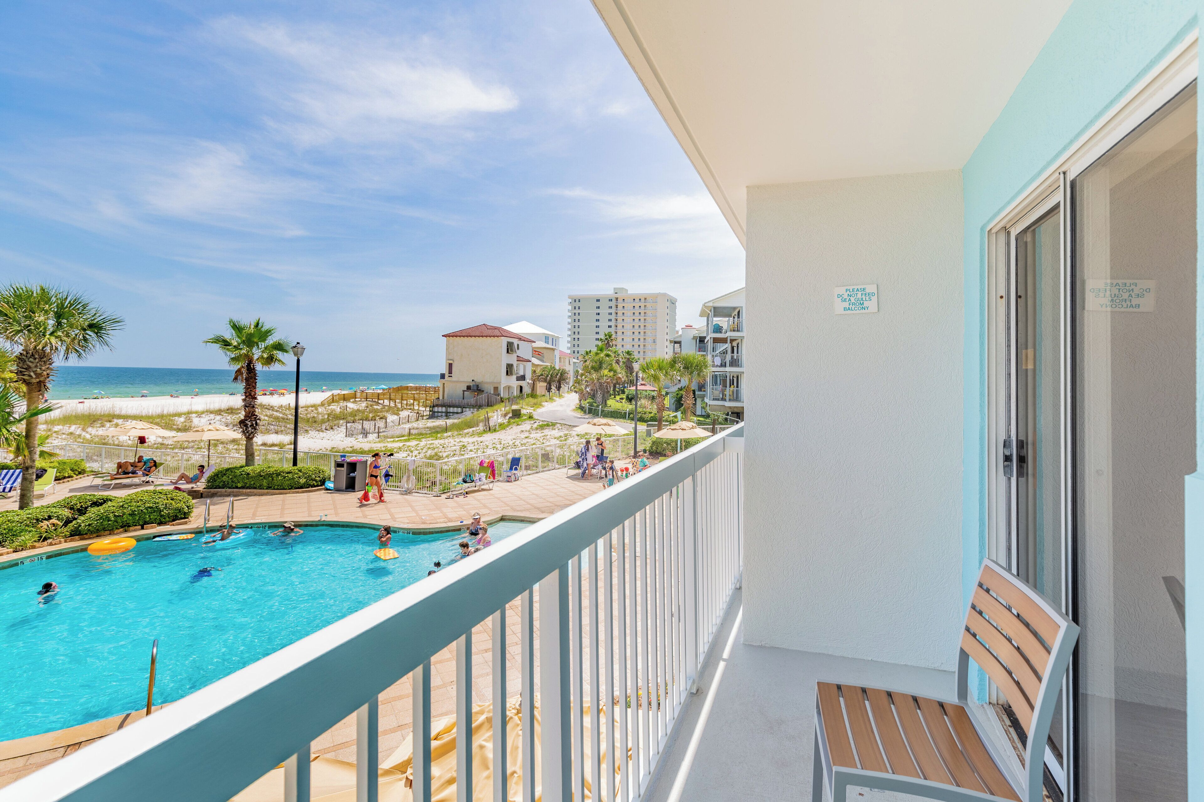 Un espace piscine avec vue sur la plage et l’océan, un balcon avec un fauteuil et un panneau sur le mur.