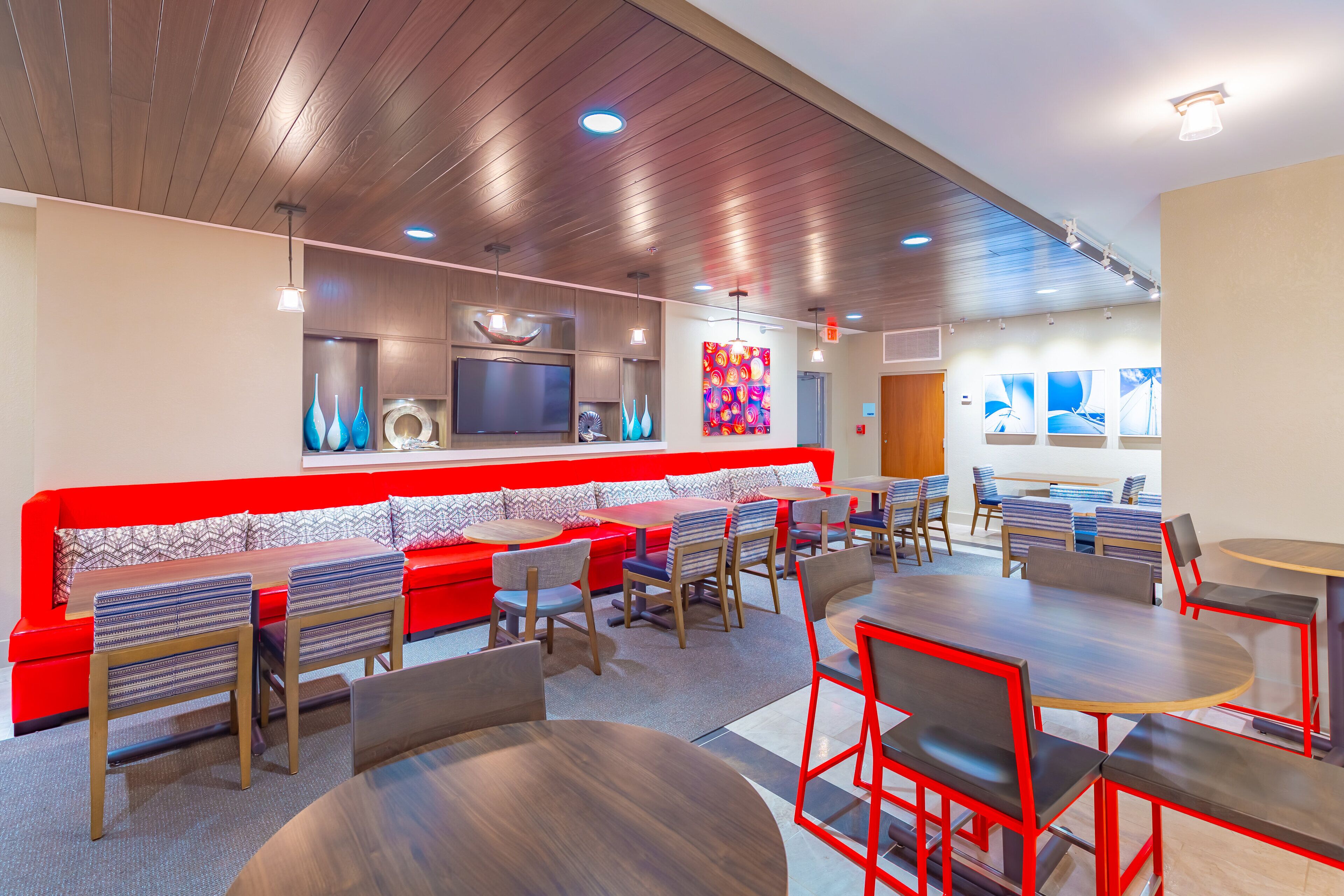 Un restaurante moderno con una decoración en rojo y blanco, que cuenta con una barra larga, varias zonas de estar y una pantalla de televisión grande.