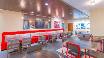 A modern restaurant with a red and white color scheme, featuring a long counter, multiple seating areas, and a large television screen.