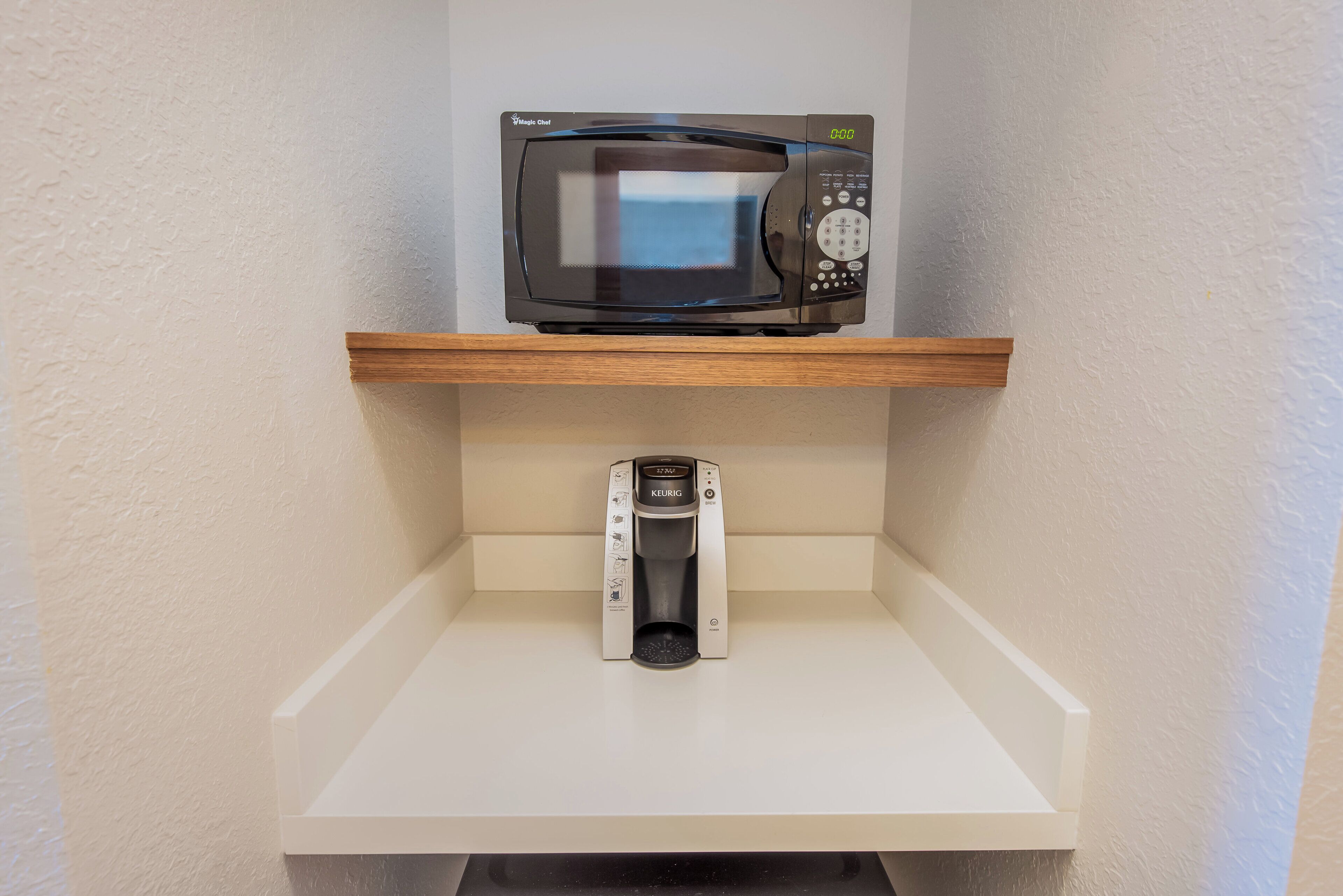 A microwave on a shelf above a coffee maker in a kitchen.