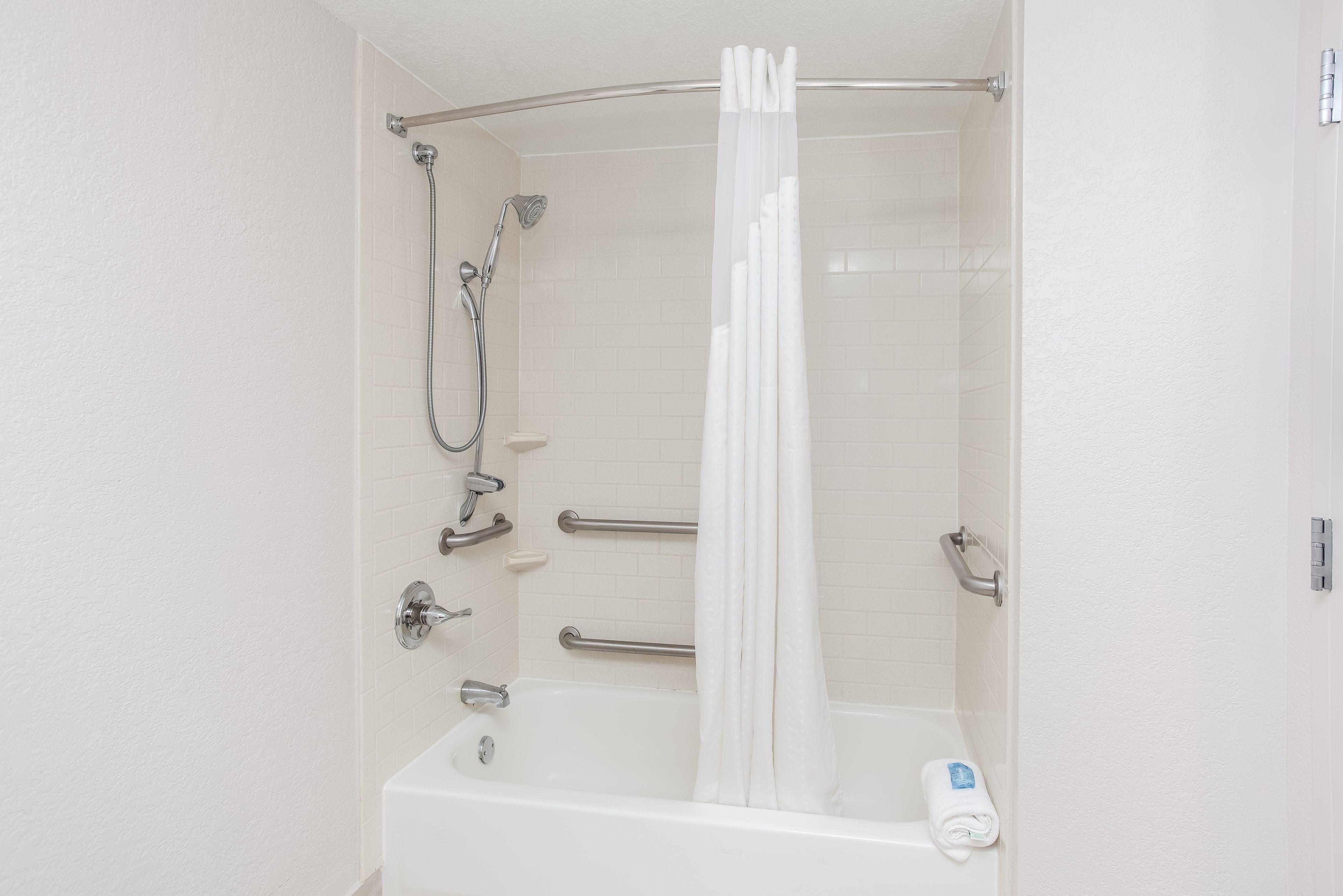 Un baño blanco con bañera, ducha y barras de apoyo.
